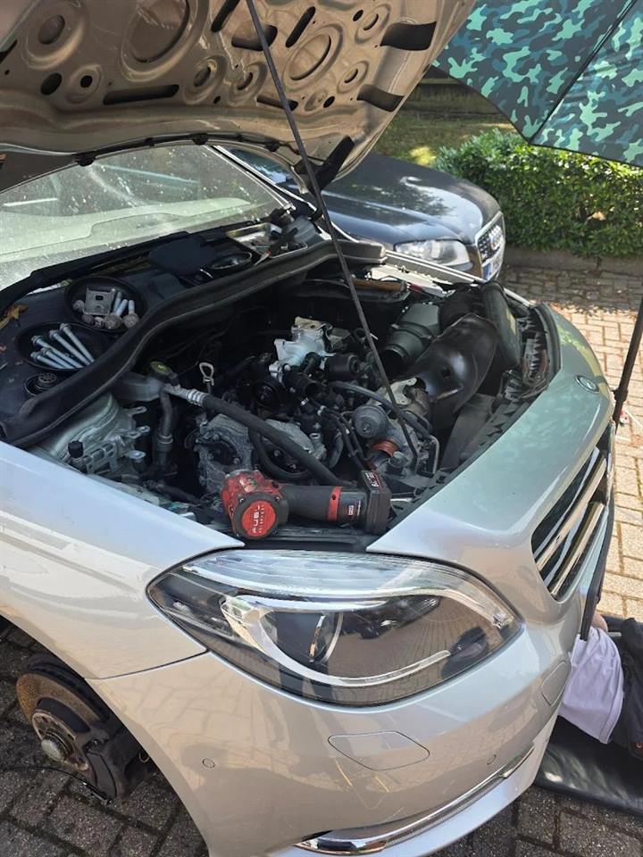Silver Mercedes with the bonnet up, engine covers off and a front wheel removed